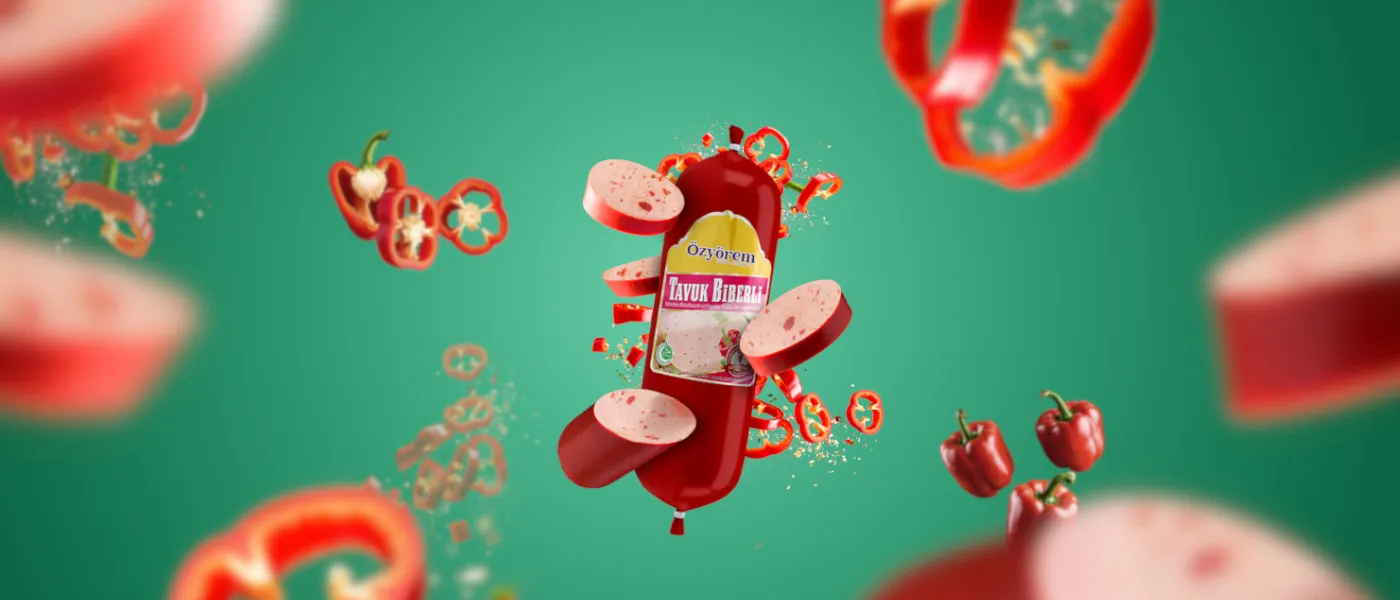 Eine rote Hähnchenfleischwurst der Marke Özyörem mit Paprikastücken (Produktname: Tavuk Biberli) schwebt auf grünem Hintergrund, umgeben von fliegenden roten Paprikascheiben und Paprikapulver. Die Wurst ist teilweise aufgeschnitten, sodass die hellrosa Wurstmasse mit roten Paprikastückchen sichtbar ist. Das Bild vermittelt Frische und Geschmack.